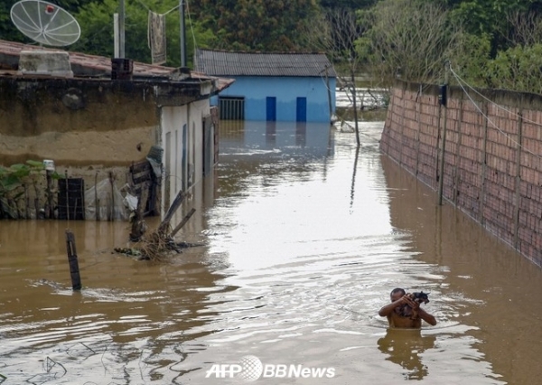 브라질 바이아주 이타페팅가에서 한 남성이 폭우로 인한 홍수 때 개를 안고 물 속을 헤매고 있다.ⓒAFPBBNews