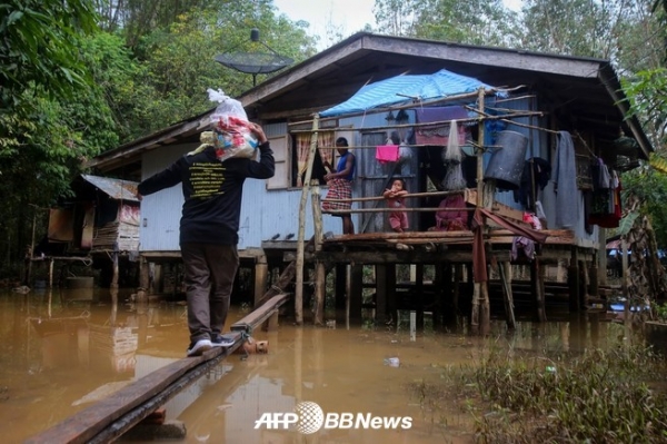 2021년 1월 16일 태국에서 몬순 폭우로 인한 홍수 피해를 입은 주민들에게 기부 물품을 전달하기 위해 한 남성이 임시 통로를 따라 기부 물품을 나르고 있다. ⓒAFPBBNews
