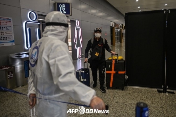 상하이 푸둥 국제공항에서 공항 보안요원이 출구를 통제하고 있는 가운데 안면 마스크를 쓴 남성이 입국하고 있다. ⓒAFPBBNews